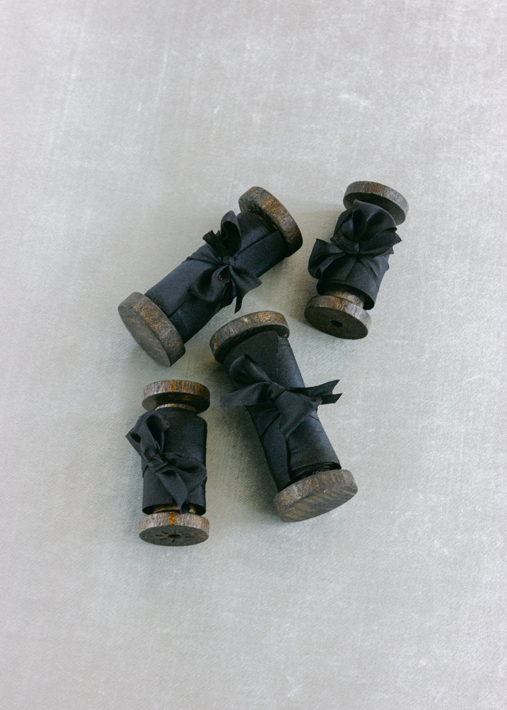 Black silk ribbon rolled onto aged wooden spools, tied with small bows and styled on a light blue velvet background
