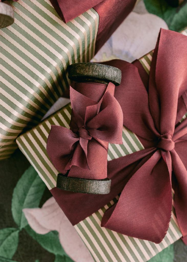 Vintage-style spools holding luxury burgundy silk ribbon, photographed for holiday wrapping and craft inspiration
