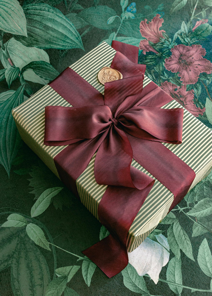 Luxury hand-dyed burgundy silk ribbon tied in a bow around a Christmas gift, styled with festive seasonal details