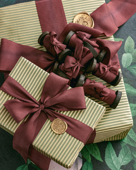 A flatlay of burgundy silk hand-dyed ribbon spilling from rustic spools, styled with beautiful wrapped holiday gifts