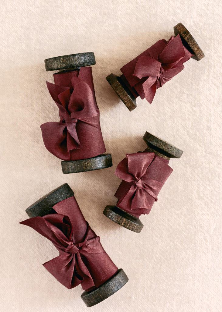 pile of Vintage-style spools holding hand-dyed burgundy silk ribbon tied up with a small bow