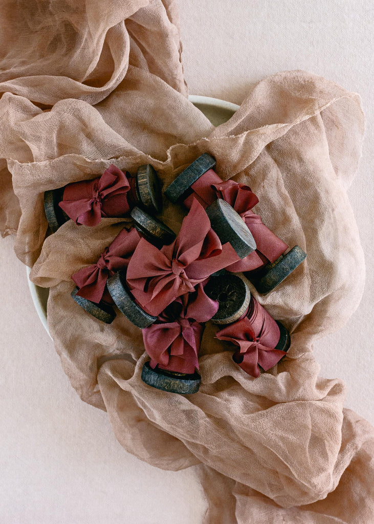 pile of Vintage-style spools holding luxury burgundy silk ribbon, photographed one soft neutral fabrics
