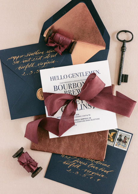 Hand-dyed burgundy silk ribbon styled on a soft backdrop, tied around fall wedding stationery with navy blue accents
