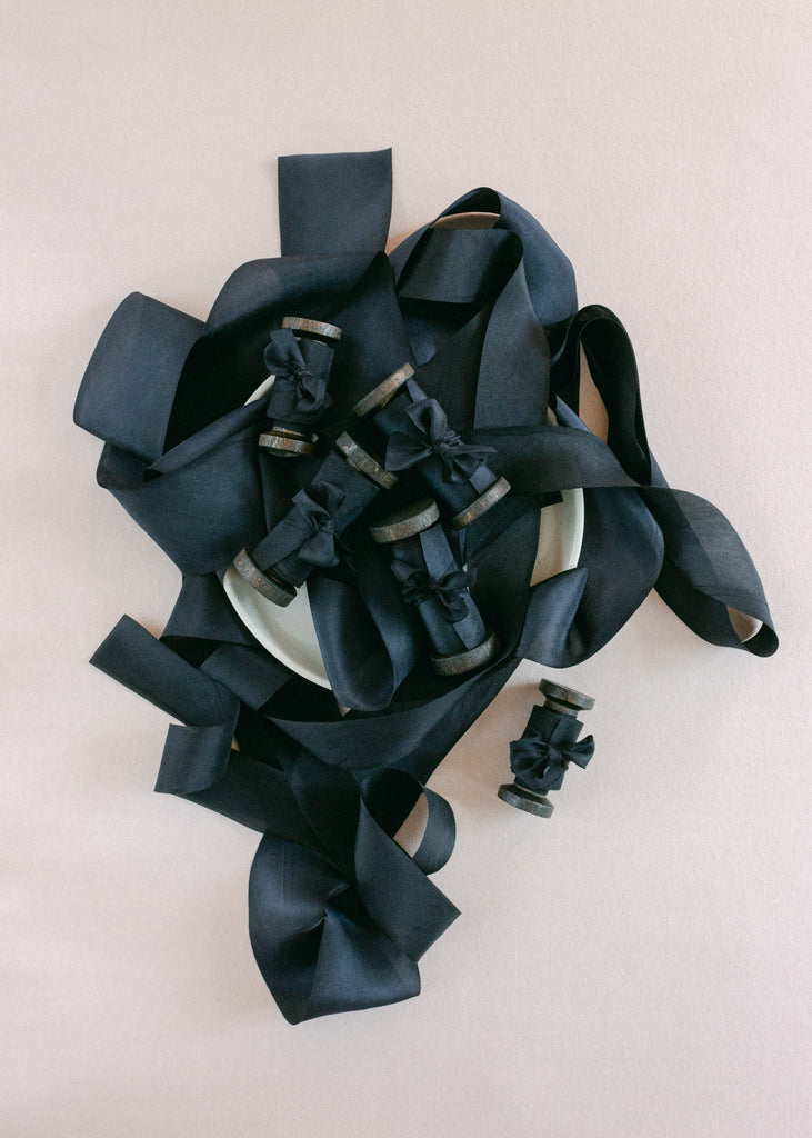 Close-up of black silk ribbon tied neatly around rustic wooden spools, displayed on a pale ceramic dish