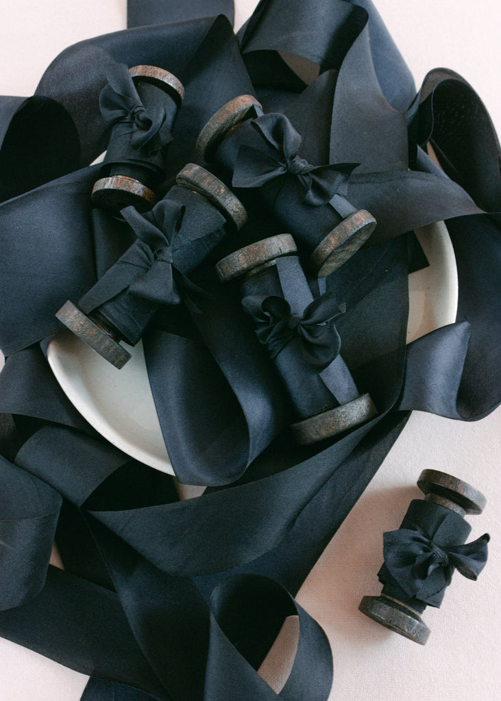 A cluster of wooden spools wrapped with matte black hand-dyed silk ribbon for wedding invitations