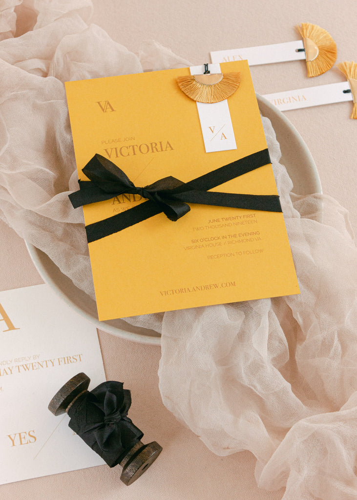 Black hand-dyed silk ribbon tied in a soft bow around a wedding invitation, styled on textured fabric for an elegant presentation