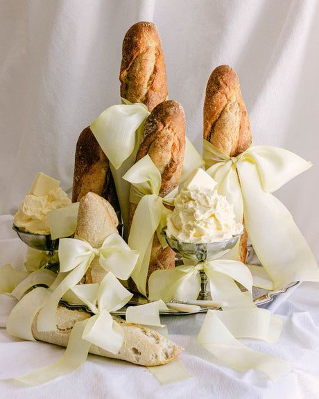 Butter yellow silk ribbon styled throughout an event bread and butter display with baguettes, vintage silver serveware, and oversized bows.