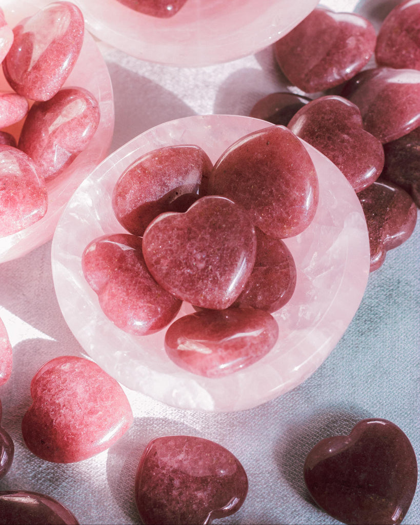 Top-down view of a Strawberry Quartz heart worry stones in crystal trinket dish, emphasizing its shiny surface and subtle red color inclusions.