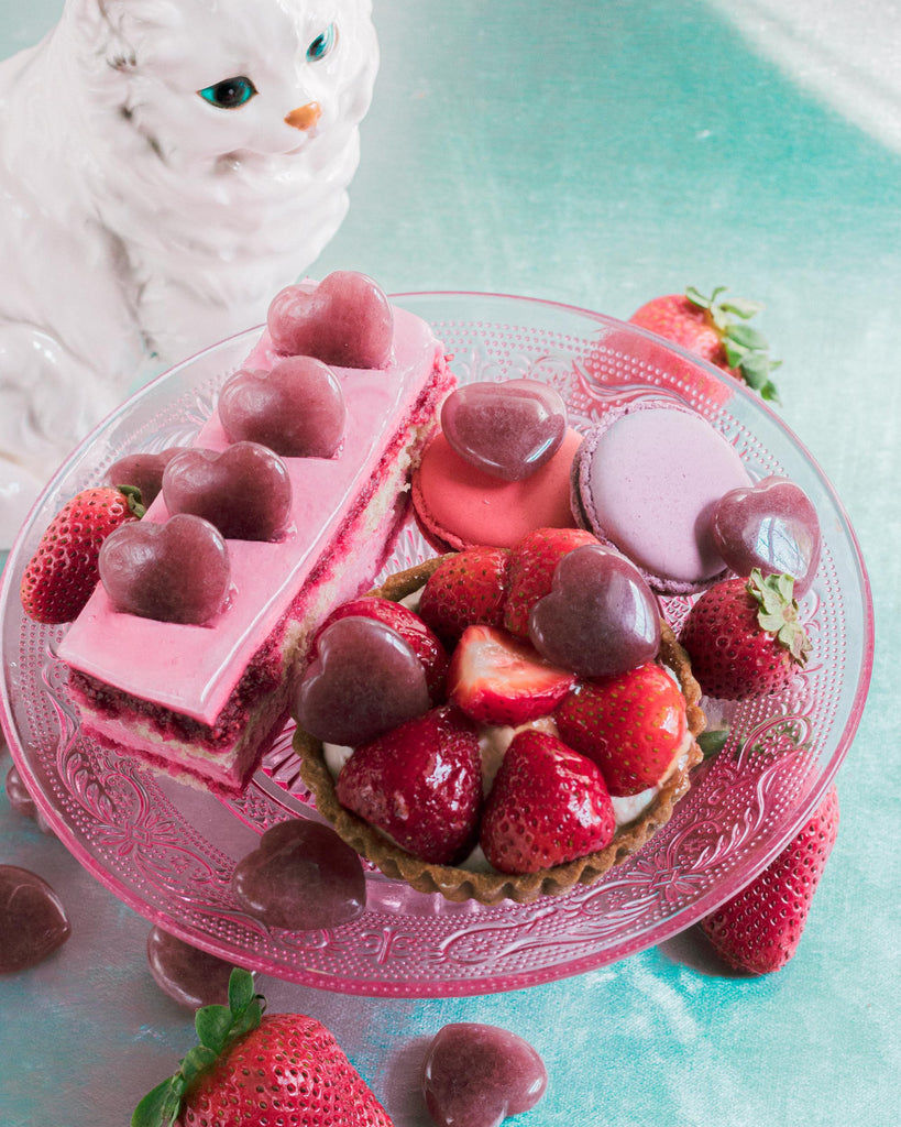 Heart-shaped Strawberry Quartz crystals artfully styled with French cakes and pastries, highlighting the stone’s  red polished sheen and delicate natural color variations.