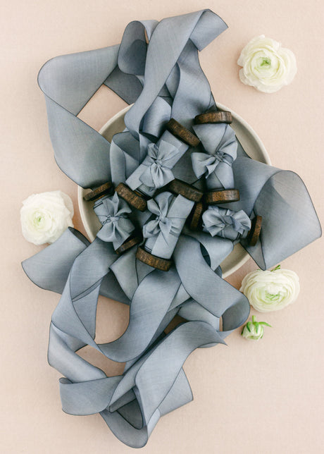 Hand-dyed dusty blue silk ribbon spooled on vintage wooden reels, styled with white ranunculus flowers for a soft wedding details