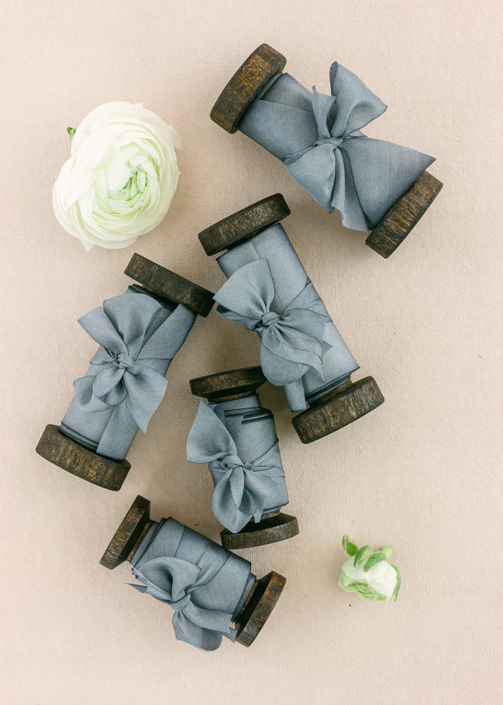 dusty blue silk ribbons wrapped around antique wood spools, displayed on blush fabric with delicate floral accent