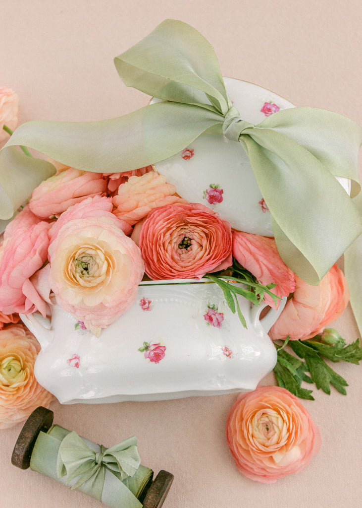 Hand-dyed sage green ribbon displayed on rustic wooden reels, ideal for wedding details and handmade crafts