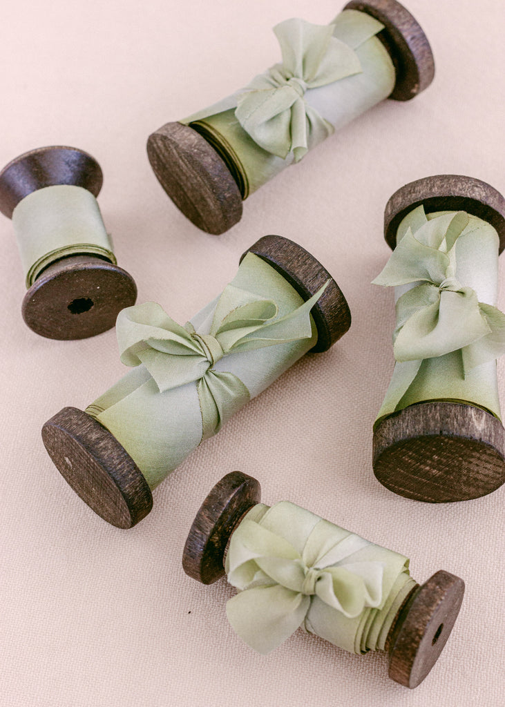 Sage green silk ribbon wrapped around vintage-style spools for wedding stationery accents