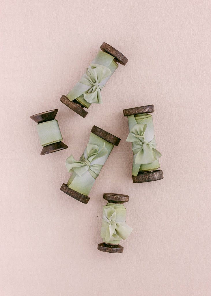 Sage green silk ribbon rolled onto antique spools, perfect for wedding stationery, crafts, and handmade projects