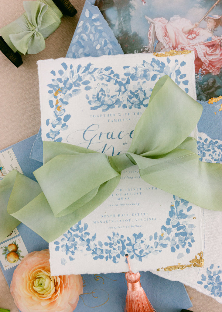 Close-up of sage green silk ribbon tied around an invitation, perfect for weddings, stationery, and crafts