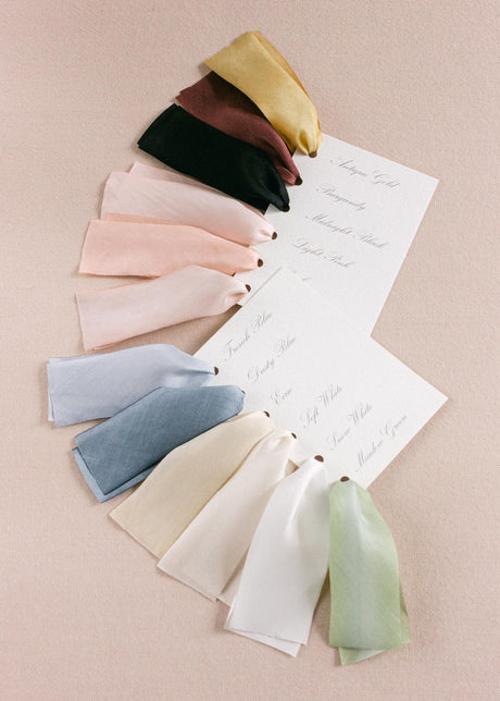 Hand-dyed silk ribbon color samples neatly arranged on a flat surface, showing a gradient of soft, vibrant hues for weddings and crafts.