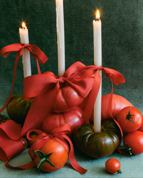 Wedding table styling with three ivory taper candles, tomato red silk bows, and flowing ribbon tails nestled among heirloom tomatoes.