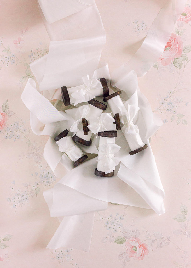 true white luxury silk ribbon on dark wood spools with flowing white ribbon around them.
