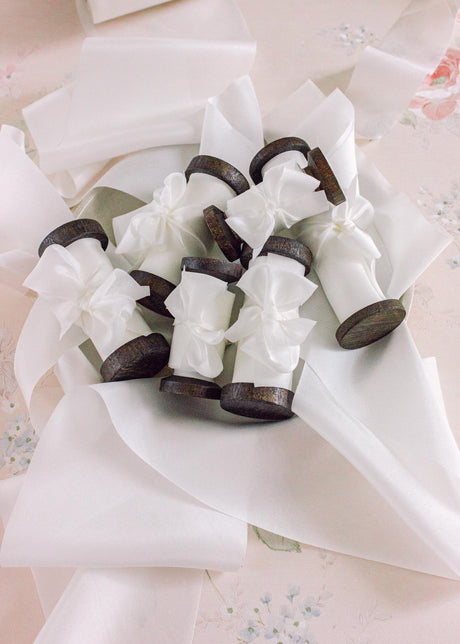 Pure white silk ribbon neatly wound on a dark wooden spool, ready for elegant wedding bouquets, invitations, or gift wrapping.