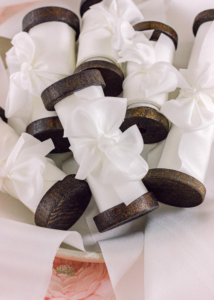 Hand-cut white silk ribbon on a dark wooden spool, showing its flowing texture and classic elegance for gift wrapping or wedding decor.