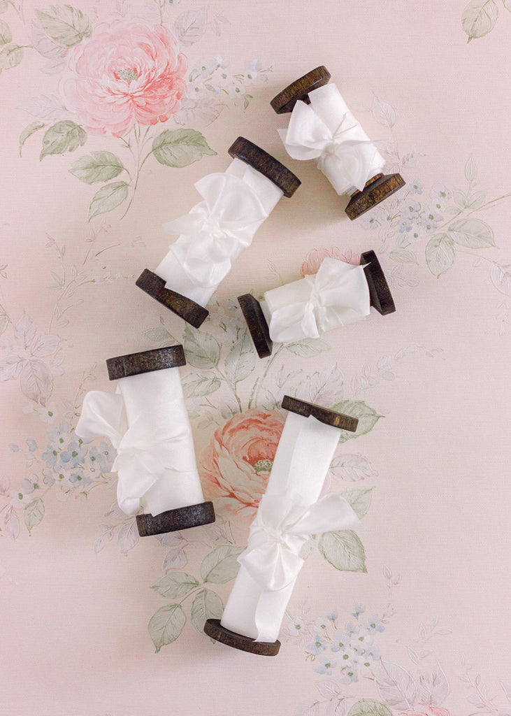 Smooth, bright white silk ribbon on a dark wooden spool, ideal for creating elegant wedding details or sophisticated gift wrapping.