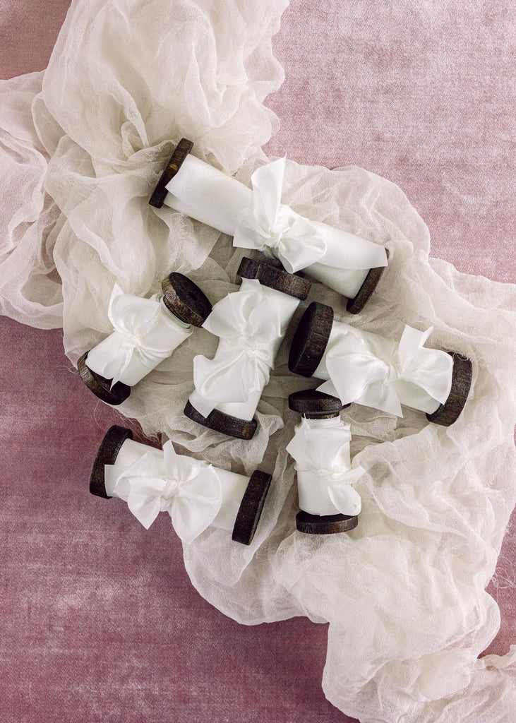 hand-dyed white silk wedding ribbons around vintage style dark wood spools with a bow.