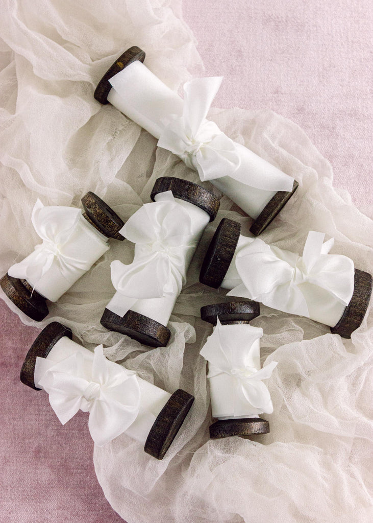 bright white silk ribbon on dark wood spools for wedding invitations.