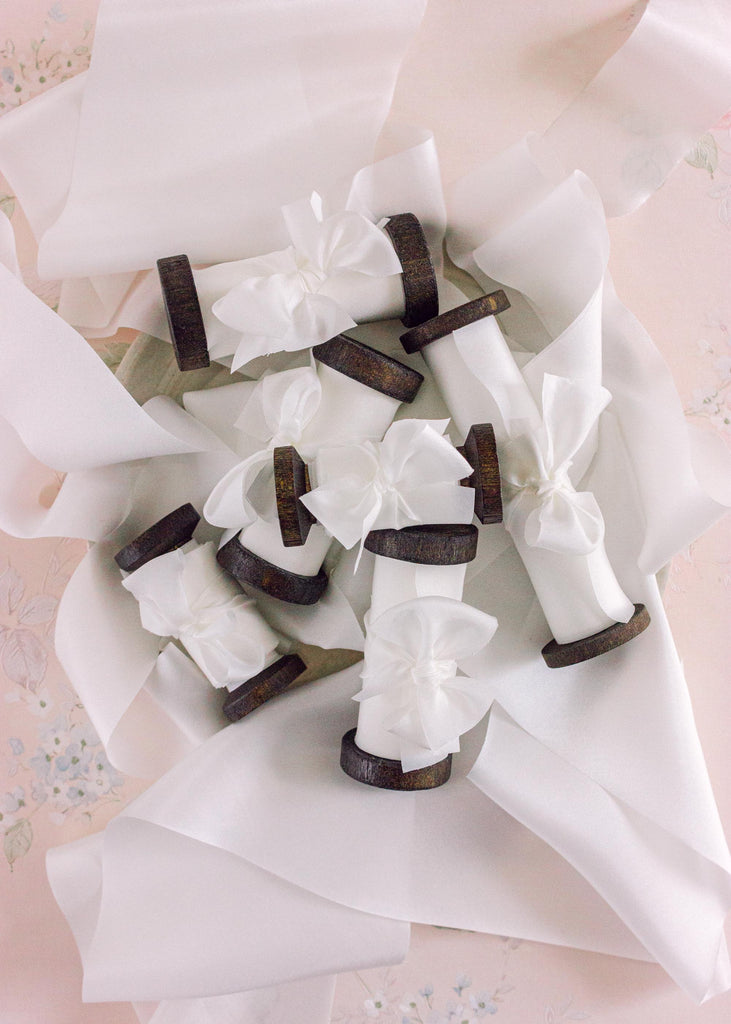 a pile of Pure white silk ribbon on a dark wooden spools, showcasing a smooth, lustrous texture for weddings and gift decor.