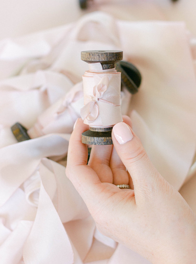 Soft pink silk ribbon rolled neatly on a spool, great for wedding bouquet ties, stationery, and romantic event décor