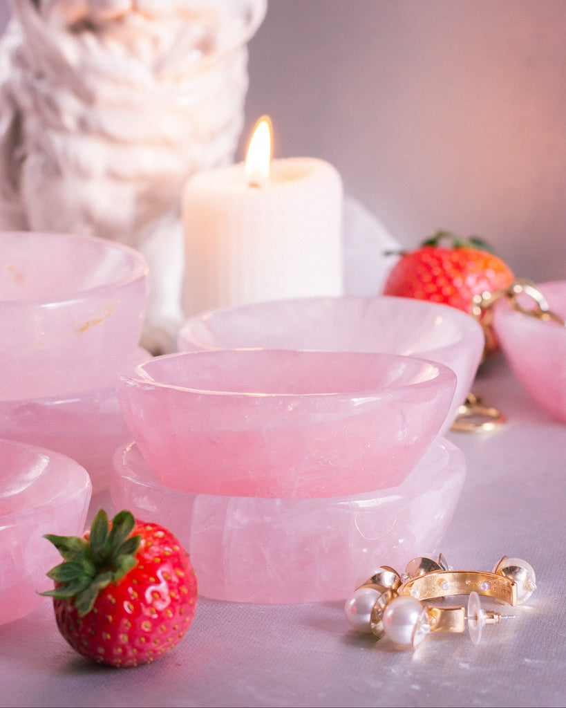 Delicate hand-carved Rose Quartz dishes in pale pink, photographed on a blue velvet surface with heart chakra crystals arranged around it.