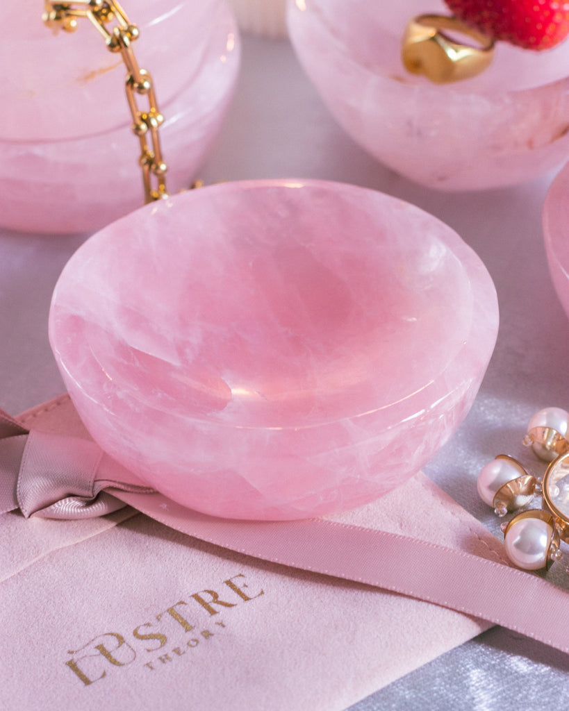 Close-up of a polished Rose Quartz crystal dish in soft pink, displayed on a textured backdrop with gitft pouch and other crystal bowls.