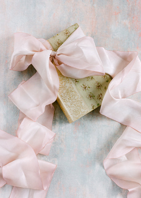 Hand dyed light pink silk ribbon elegantly tied in a big bow around a vintage book, perfect for wedding invitations and romantic event styling